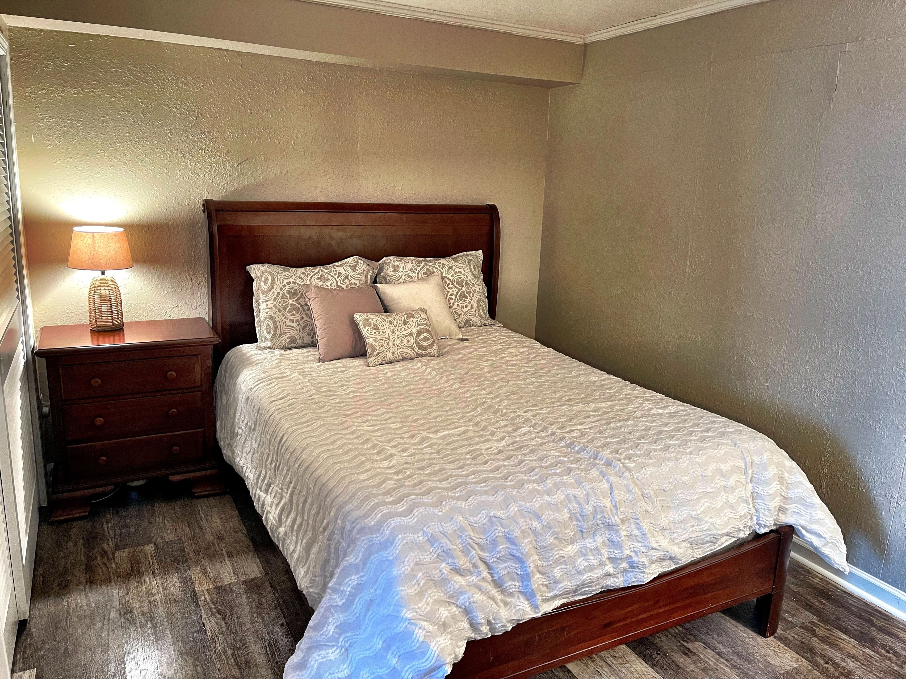 A neatly made bed with patterned bedding, a wooden nightstand with a lamp, and a wooden floor.