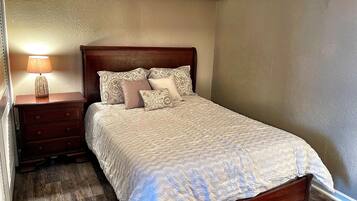 A neatly made bed with patterned bedding, a wooden nightstand with a lamp, and a wooden floor.