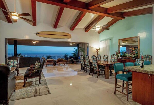 Un'ampia zona giorno con vista sull'oceano, arredamento in legno e una ventola a soffitto.