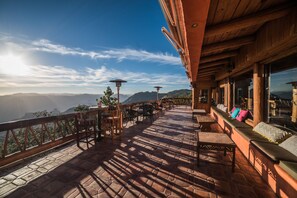 Una terraza con vistas a montañas, mobiliario de madera y una barandilla.