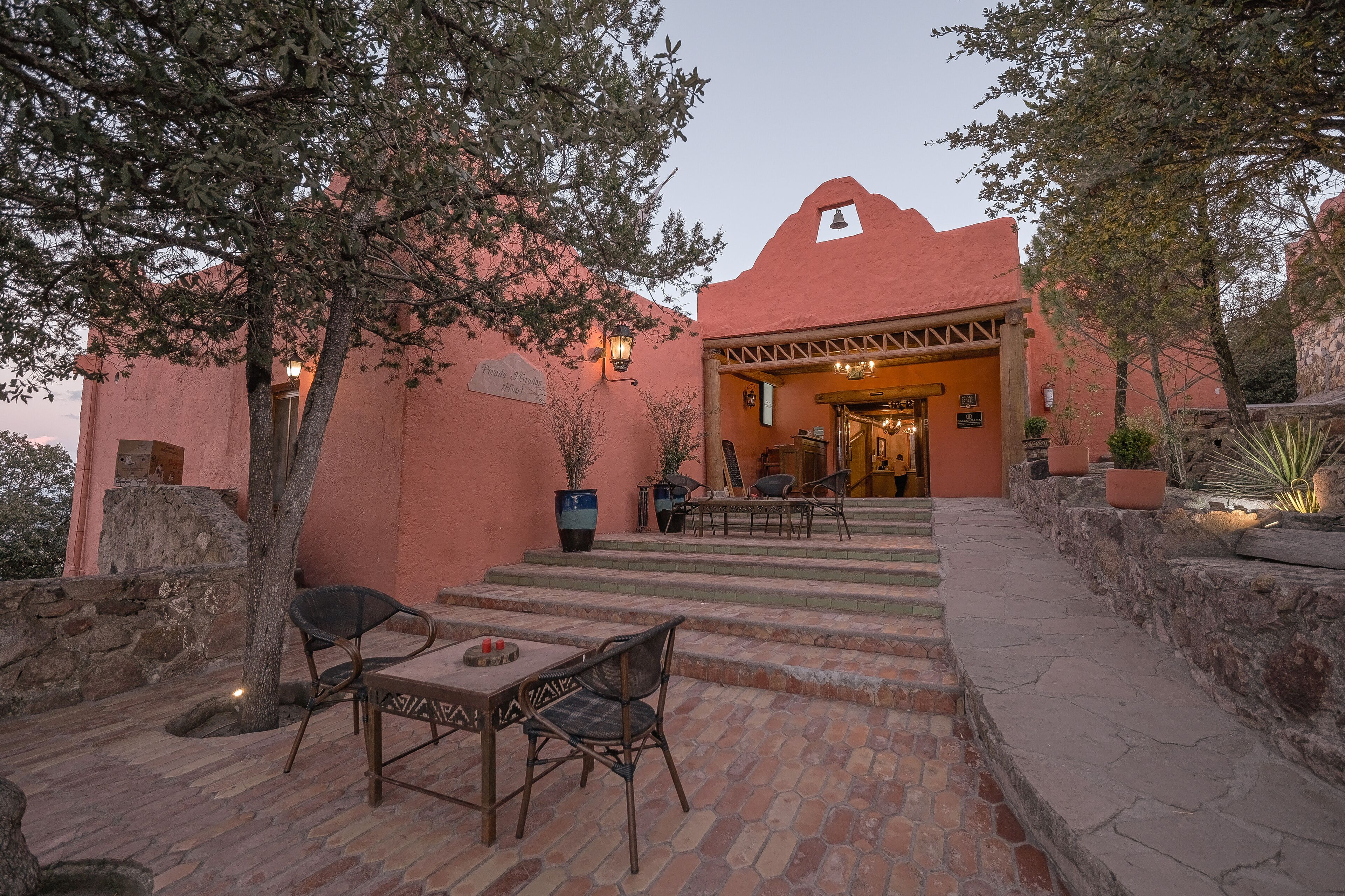 A building with a red facade, outdoor seating area with chairs and a table, and a staircase leading to the entrance.