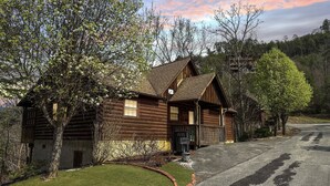Eine Holzhütte mit Veranda und Garage, umgeben von Bäumen und einem Rasen.