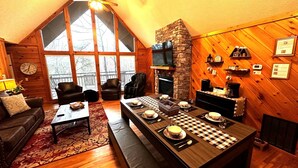 Ein gemütliches Wohnzimmer mit Kamin, einem Esstisch für vier Personen und einem großen Fenster mit Blick ins Freie.