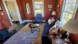 A cozy living room with a blue armchair, a sofa with cushions, a coffee table, and a lamp.
