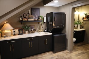 A modern kitchen with dark cabinetry, a built-in refrigerator, and a countertop with various items. - Parker's Point by Creative Cabins (Logan)