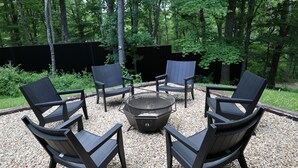 A circular seating arrangement with a central fire pit, surrounded by a gravel area, and enclosed by a wooden fence. - Parker's Point by Creative Cabins (Logan)
