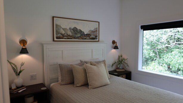 A bedroom with a bed, bedside tables, a painting, and a window with a view. - Parker's Point by Creative Cabins (Logan)