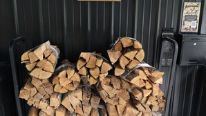 A stack of firewood labeled 'FIREWOOD' in front of a black metal wall. - Parker's Point by Creative Cabins (Logan)