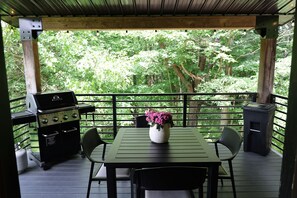 A covered outdoor area with a table, chairs, a grill, and a trash can.