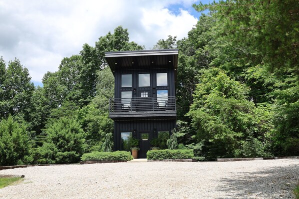 A modern two-story building with a balcony, surrounded by dense greenery.