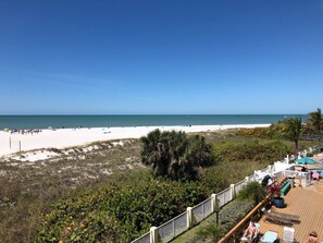 Vista de una playa con una terraza de madera, sillas de descanso y sombrillas.