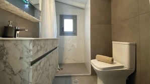 Un baño moderno con tocador de mármol, inodoro y zona de ducha.