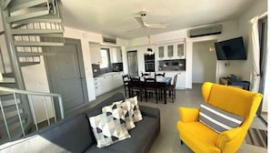 Una sala moderna con un sofá, un sillón amarillo y un comedor con una mesa y sillas.