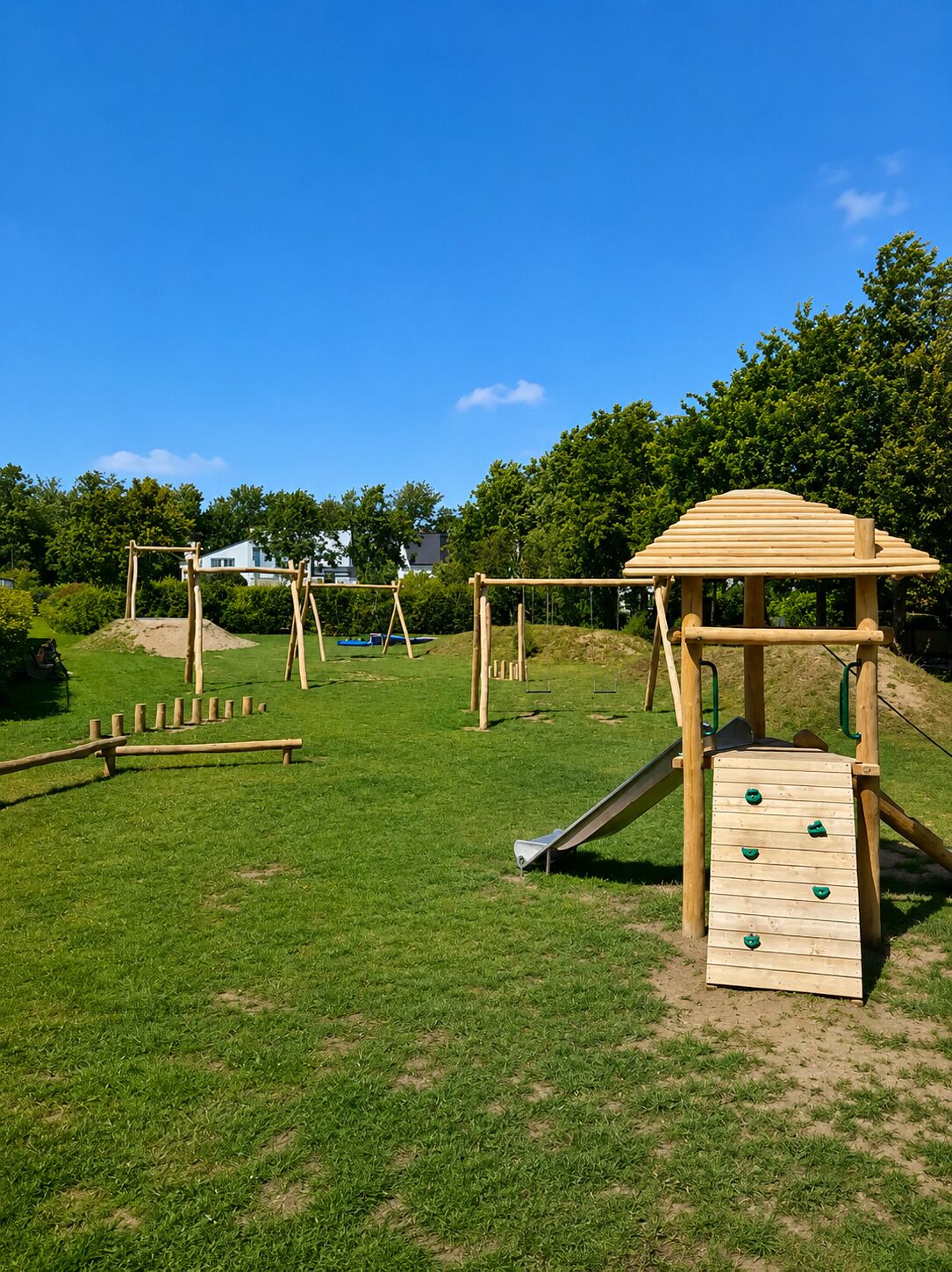 Une aire de jeux avec une structure d’escalade en bois, des balançoires et un toboggan.
