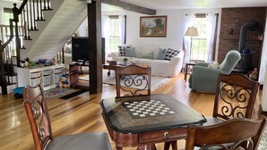 A cozy living room with a wooden staircase, a fireplace, and a chess table. - 4bdrm Cottage central to year round fun w/fireplace (Weston)