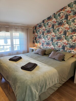 Une chambre à coucher avec un lit, des oreillers, une table de chevet et un papier peint à motifs floraux.