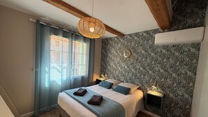 Une chambre à coucher comprenant un lit, deux tables de chevet, un luminaire suspendu, une fenêtre avec des rideaux et un mur décoré d’un motif.