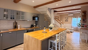 Une cuisine spacieuse dotée d’un îlot central, de meubles de couleur grise, de poutres en bois et d’un parquet disposé en motif à chevrons.