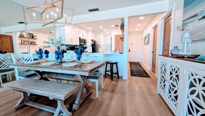 A spacious dining area with a wooden table set for four, a chandelier, and a view into the kitchen. - Adorable 2nd floor Villa with Peek-a-Boo Gulf Views (Panama City Beach)