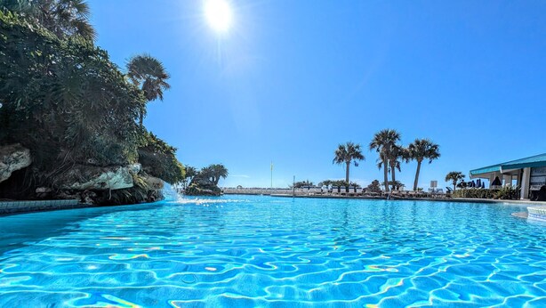 A clear blue pool with a rocky cliff and palm trees in the background. - Adorable 2nd floor Villa with Peek-a-Boo Gulf Views (Panama City Beach)