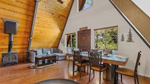 A cozy, sloped-roofed room with a wooden interior, a dining table with chairs, a sofa, and a fireplace. - Nakai Trail Vacation Rental | 4-BR A-Frame in Kachina Village, Flagstaff | Loft • Firepit  • Game Rm • Sauna • New Bathroom (Flagstaff)