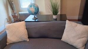 A gray sofa with two beige pillows, a globe, a small potted plant, and a radiator in the background. - The East Loft at Dartmouth Avenue *New 1 Bed-Apt. (Providence)