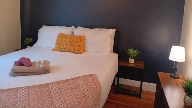 A neatly made bed with a patterned bedspread, two pillows, and a rolled towel. There is a small bedside table with a lamp and a plant. - The East Loft at Dartmouth Avenue *New 1 Bed-Apt. (Providence)