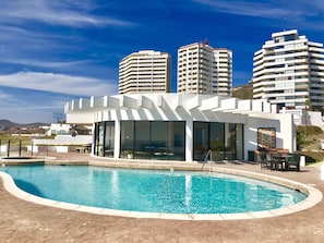 A modern hotel with a pool area, large windows, and a view of surrounding high-rise buildings.