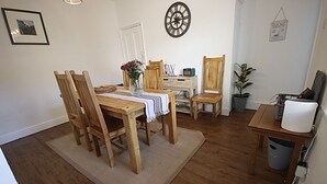 Un comedor con mesa y sillas de madera, un florero con flores, un reloj y un cartel que anuncia vela.