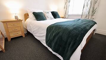 A neatly made bed with a green quilt, a wooden bedside table with drawers, and a lamp.