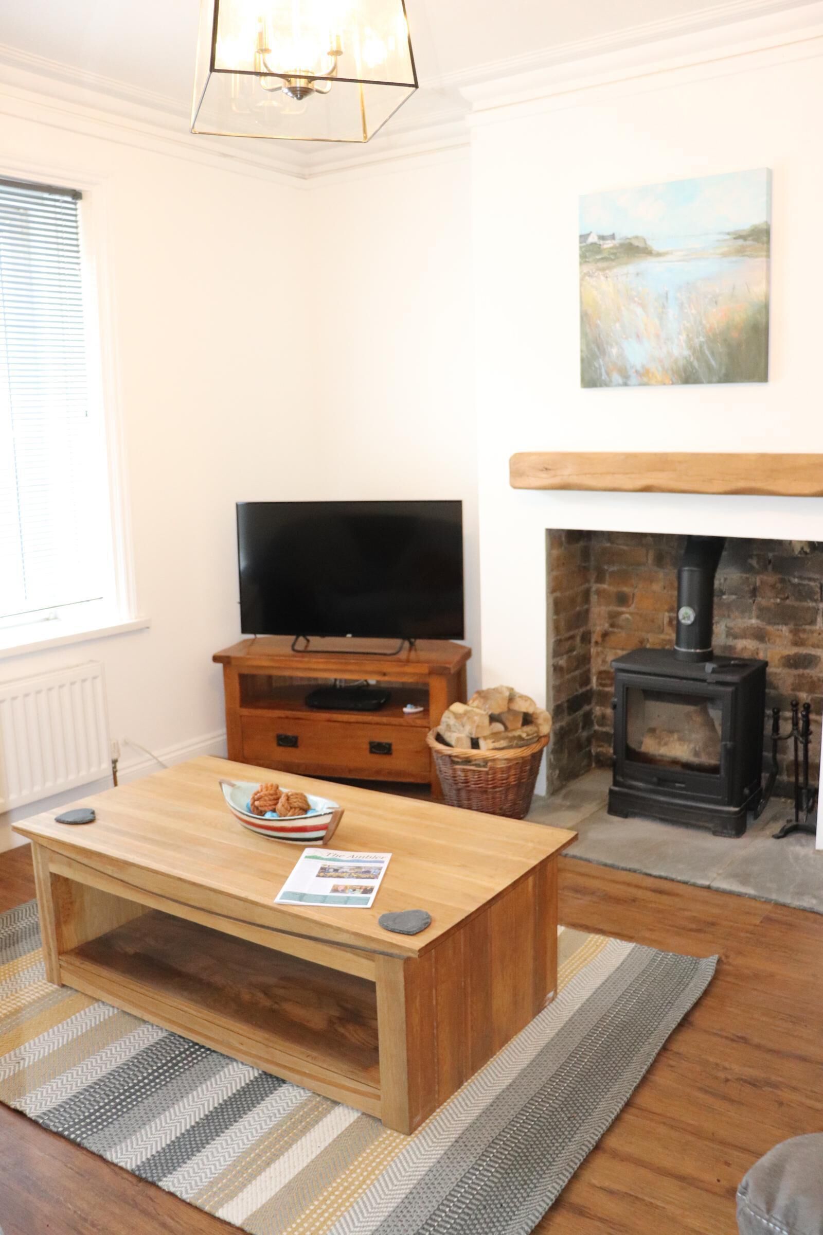 A cozy living room with a wooden coffee table, a flat-screen TV on a wooden stand, a fireplace with a stone surround, and a painting on the wall.