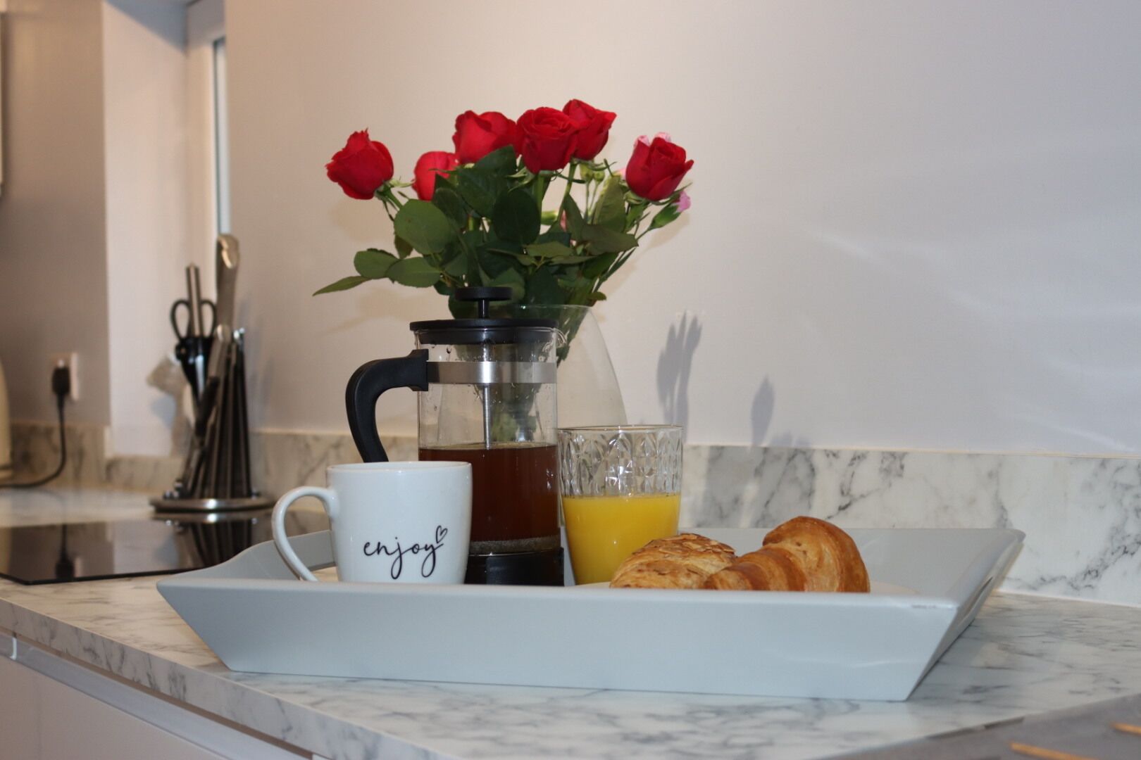 A kitchen counter with a coffee maker, a mug, a glass of orange juice, and a plate with croissants.