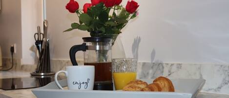 A kitchen counter with a coffee maker, a mug, a glass of orange juice, and a plate with croissants.