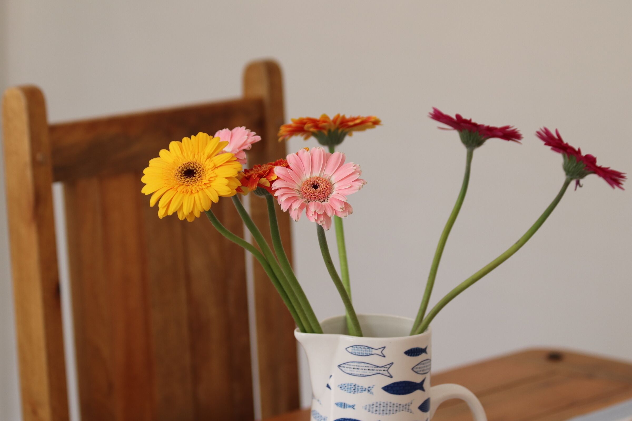 A white vase with blue fish patterns containing pink and yellow flowers.