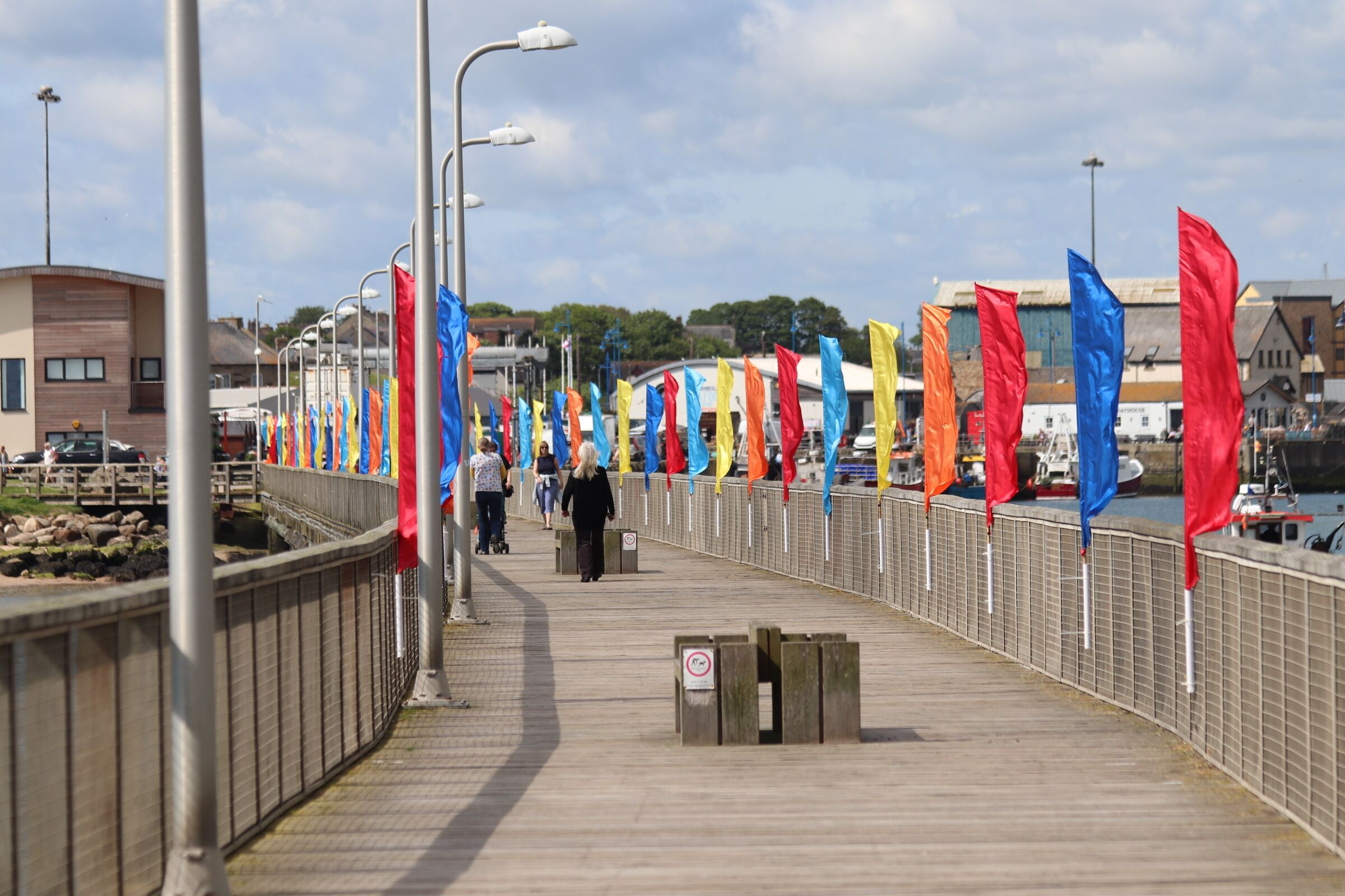 A pedestrian walkway lined with colorful flags, a metal railing, and a clear sky.