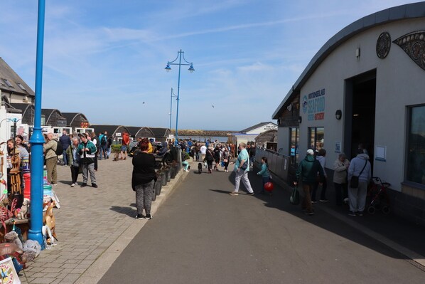 A busy boardwalk with shops and a seafood restaurant. - Kindly Light Cottage (Morpeth)