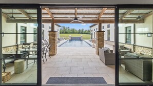Ein Außenbereich mit Terrasse, Pool, steinernen Säulen, Korbmöbeln und Blick auf ein Wohngebäude im Hintergrund.