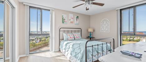 Un dormitorio con cama, mesita de noche, ventilador de techo y vistas al exterior.
