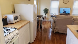 Cocina compacta con estufa a gas, microondas, refrigerador, encimeras de madera y un comedor con una planta y un televisor.