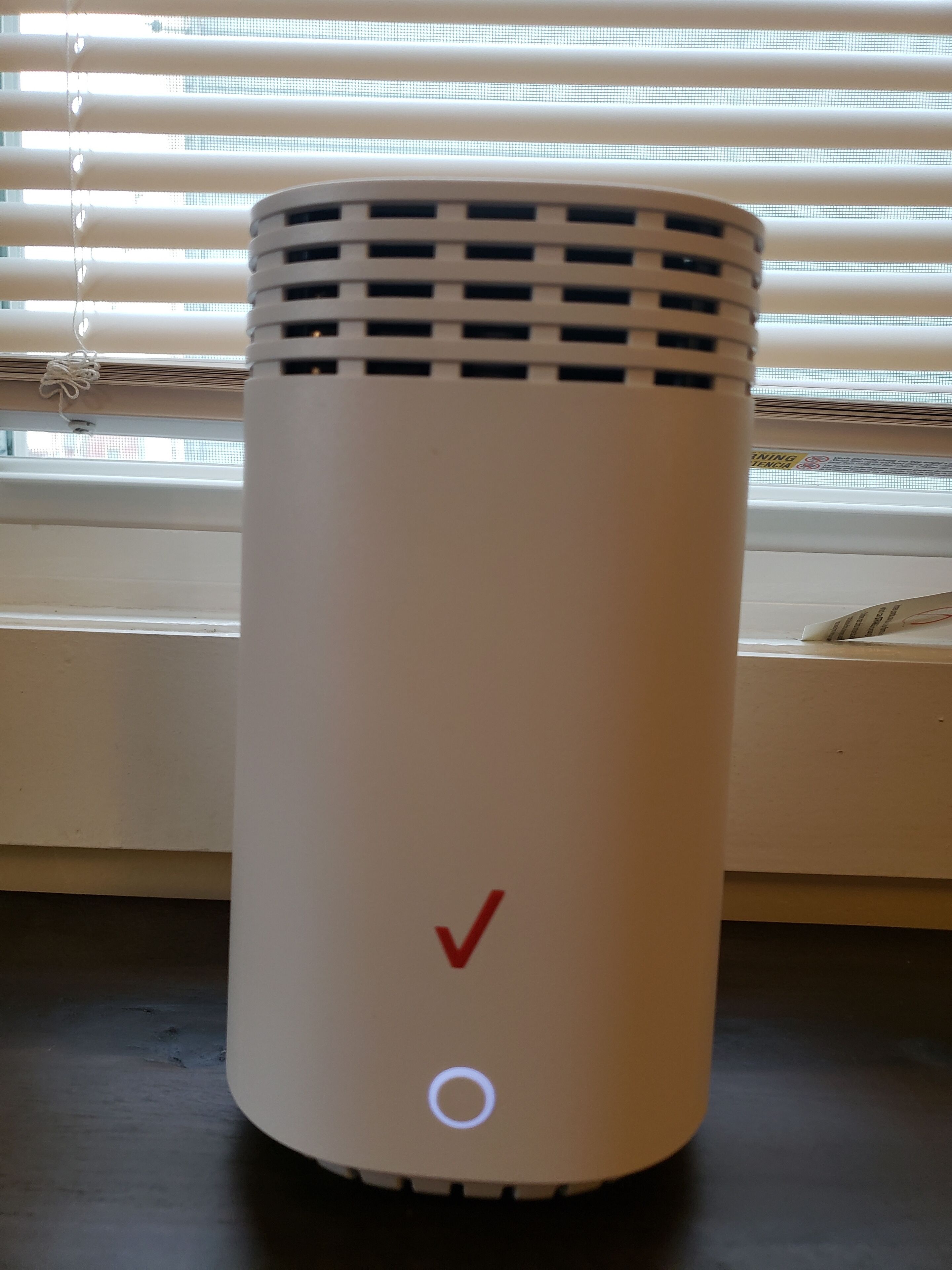 A white cylindrical device with a vented top, a red check mark, and a circular button on a flat surface.