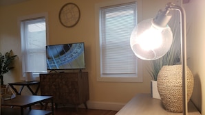 Una sala de estar con televisión, lámpara, aparador de madera y un jarrón grande.