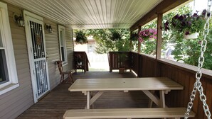 A covered porch with wooden benches and tables, a wooden railing, and hanging flower baskets. - Conveniently located 2 bedroom home only minutes from hiking and state park fun! (Warren)