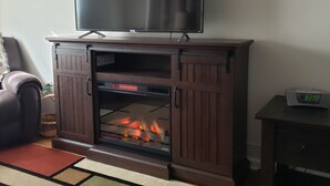 A living room with a fireplace, a television mounted above it, and a clock on a side table. - Conveniently located 2 bedroom home only minutes from hiking and state park fun! (Warren)