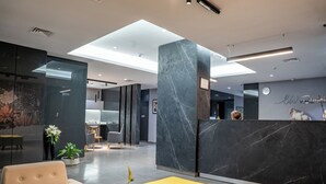 A modern reception area with a marble reception desk, a seating area with a yellow ottoman, and a wall-mounted clock. - Liv weibdeh (Amman)