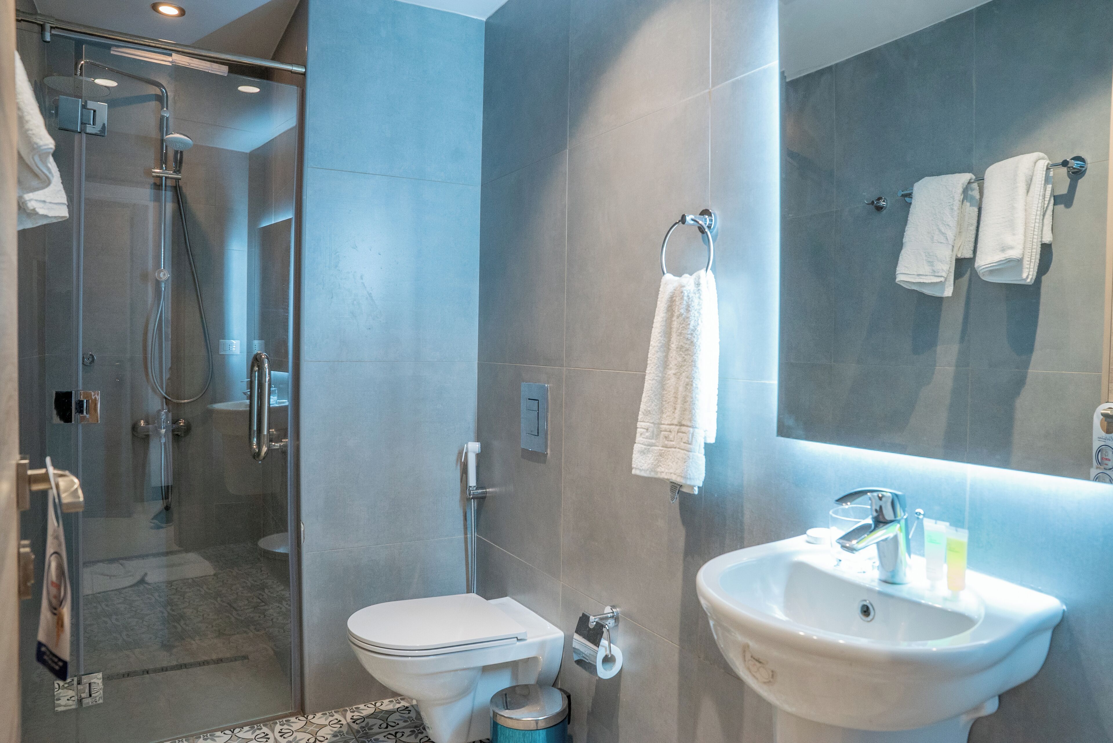 A modern bathroom with a glass shower enclosure, a white toilet, a sink with a mirror, and a towel rack with towels.