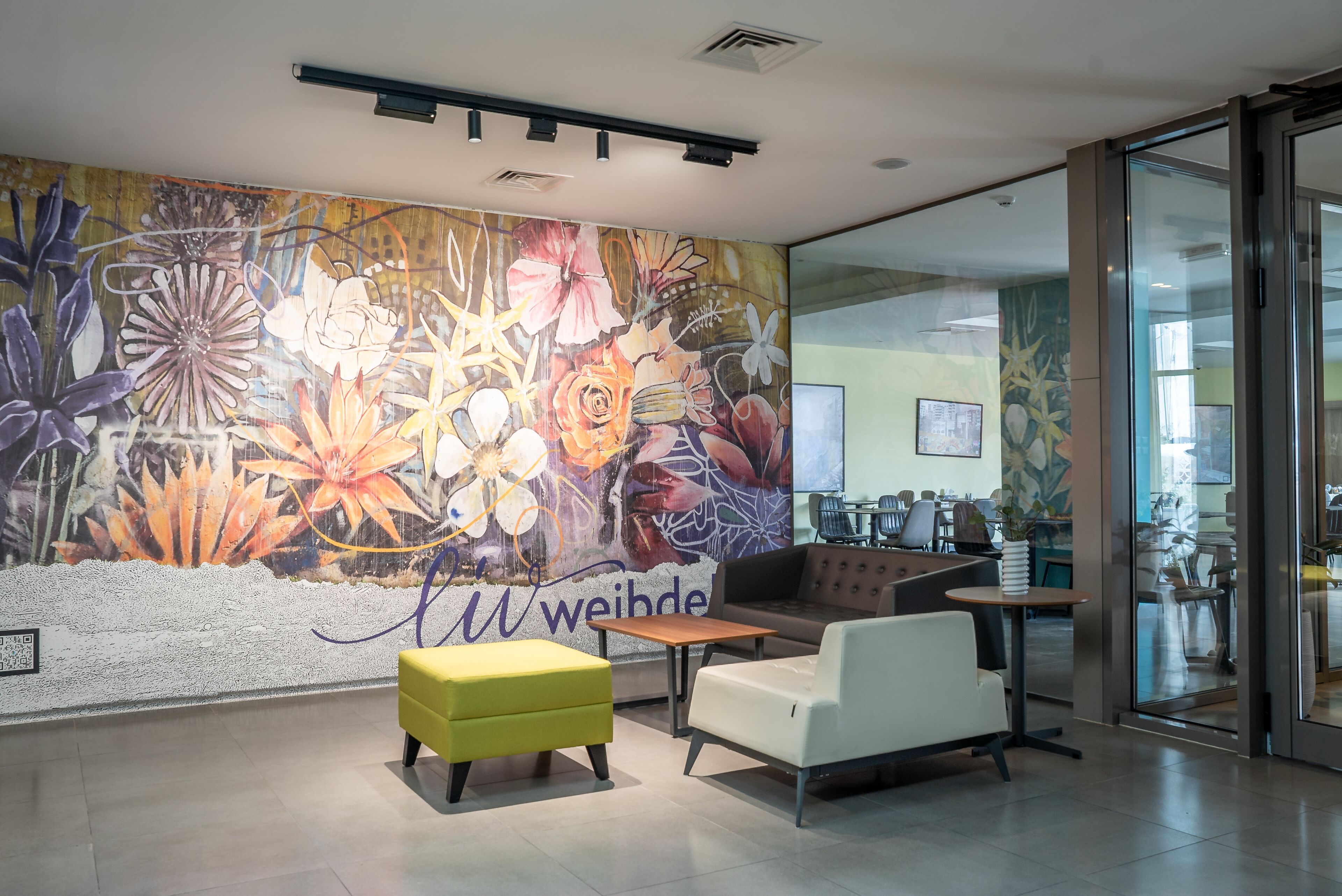 Een modern interieur met een bloemenmuur, zithoek en een glazen deur die naar een andere ruimte leidt.