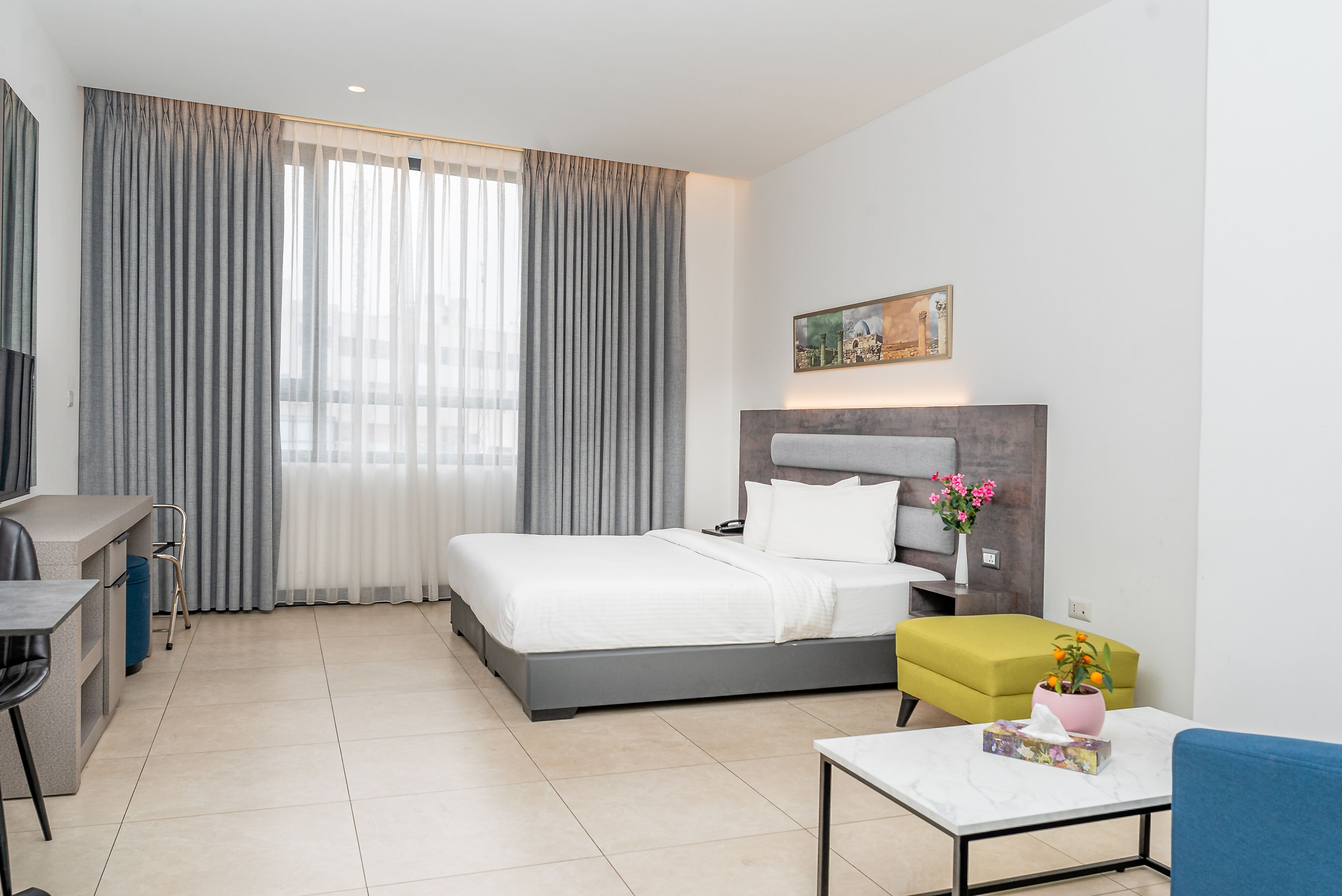 Una habitación de hotel moderna con cama, escritorio, silla, mesita y un cuadro en la pared.