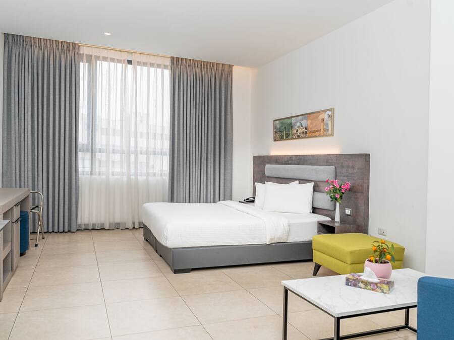 Una habitación de hotel moderna con cama, escritorio, silla, mesita y un cuadro en la pared.