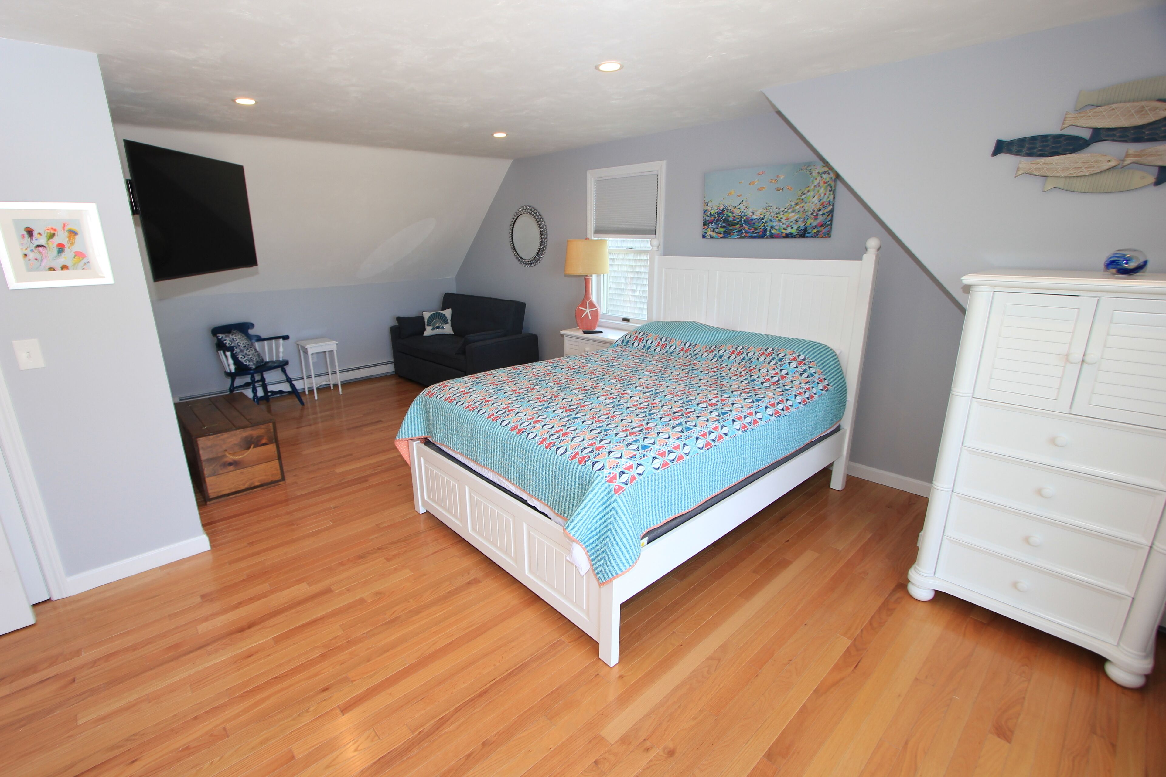 A bedroom with a bed, dresser, chair, and artwork on the walls.
