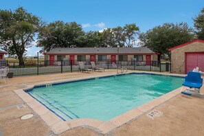 A swimming pool with lounge chairs and a fenced area, surrounded by a building with red doors and a brick structure. - Americas Best Value Inn Lockhart (Lockhart)